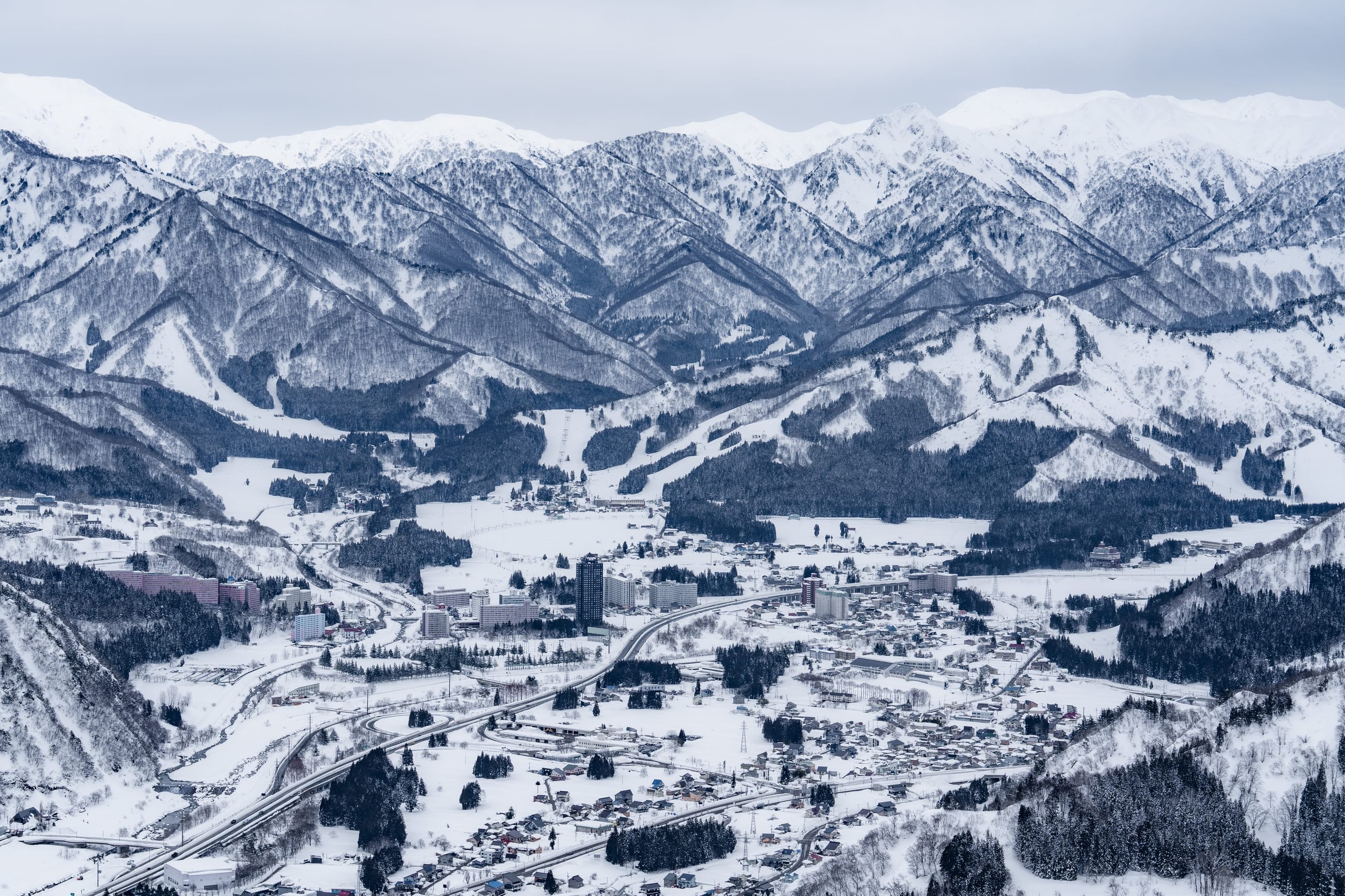 从高处俯瞰积雪山谷、村庄与层叠群山。