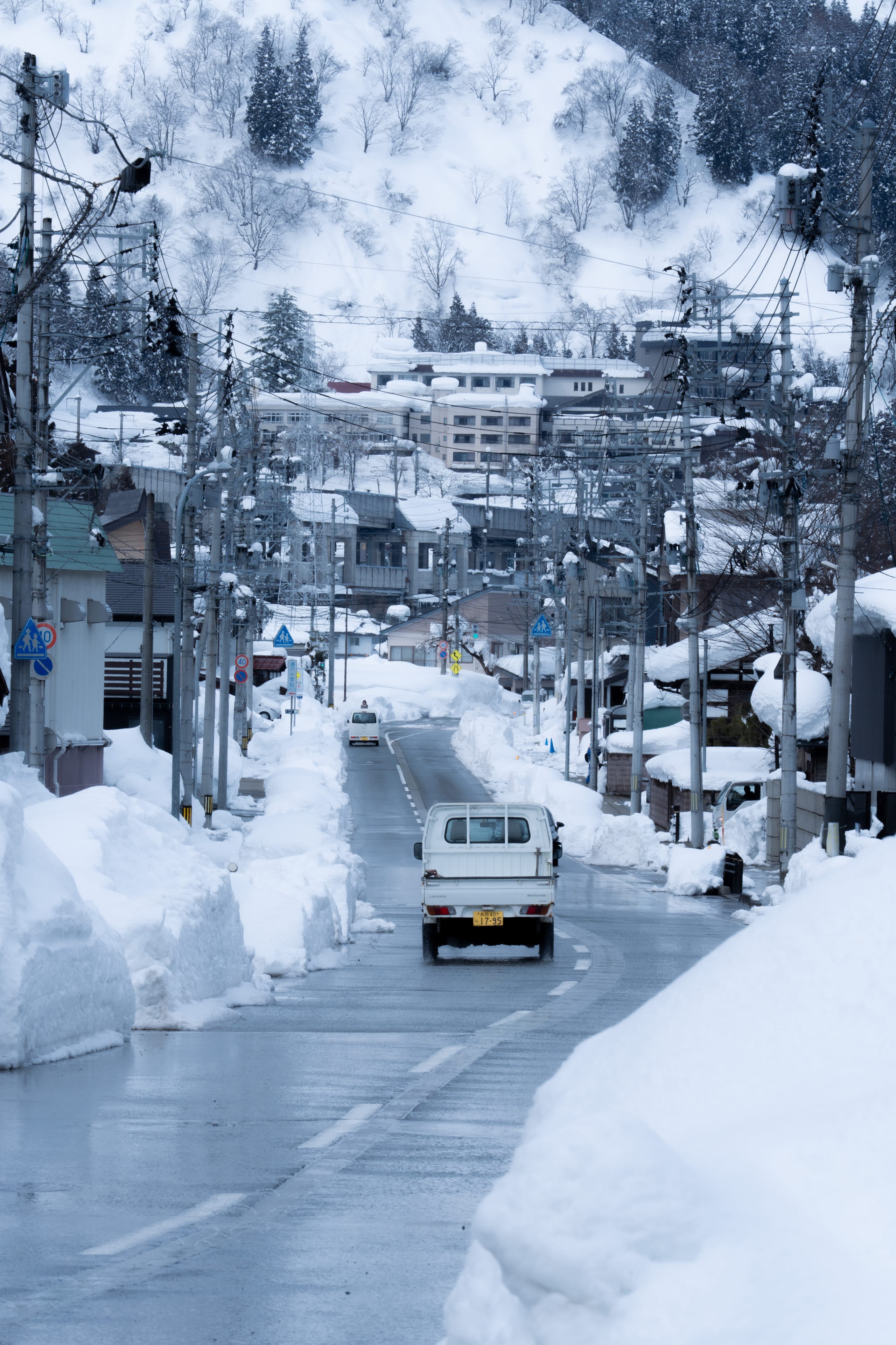 小型车辆沿积雪覆盖的山城道路向远处驶去。