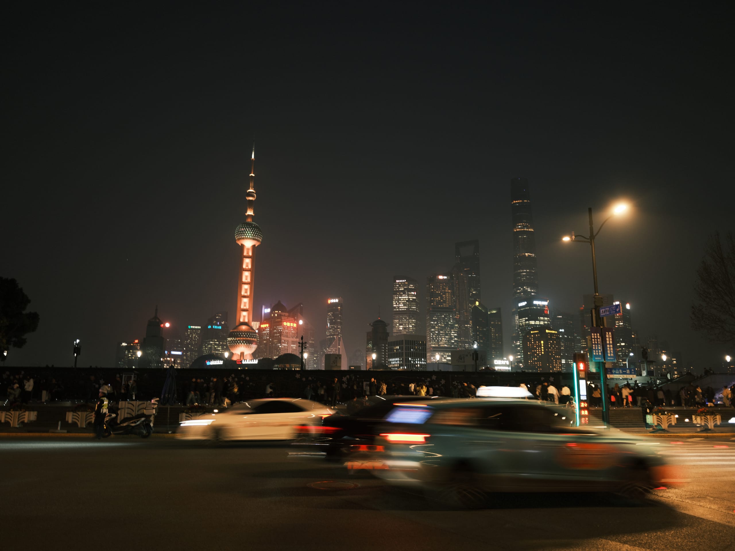 深色夜空下的城市高楼，前景汽车驶过街道。