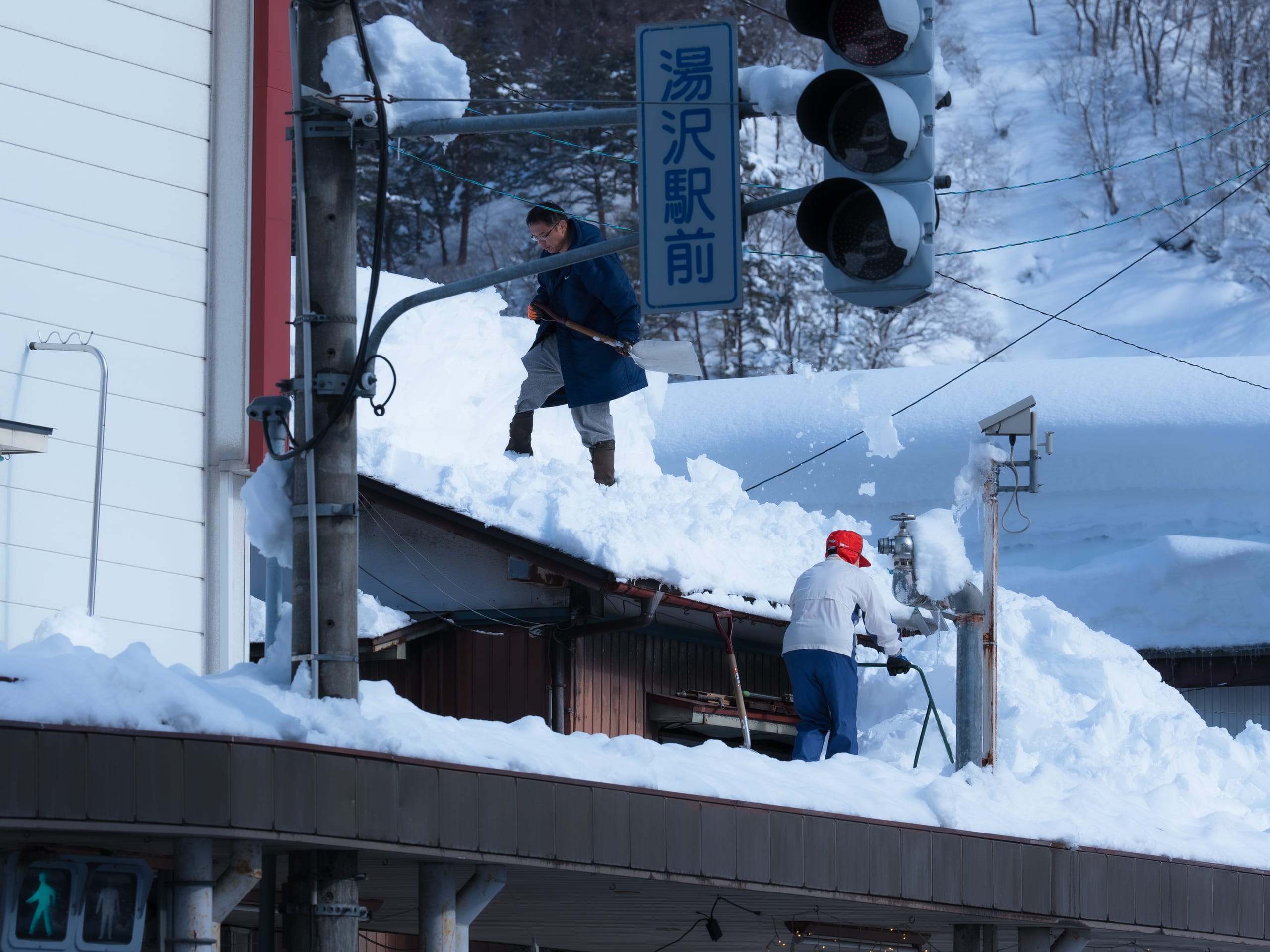 两个人在深雪覆盖的屋顶和街边清理积雪。
