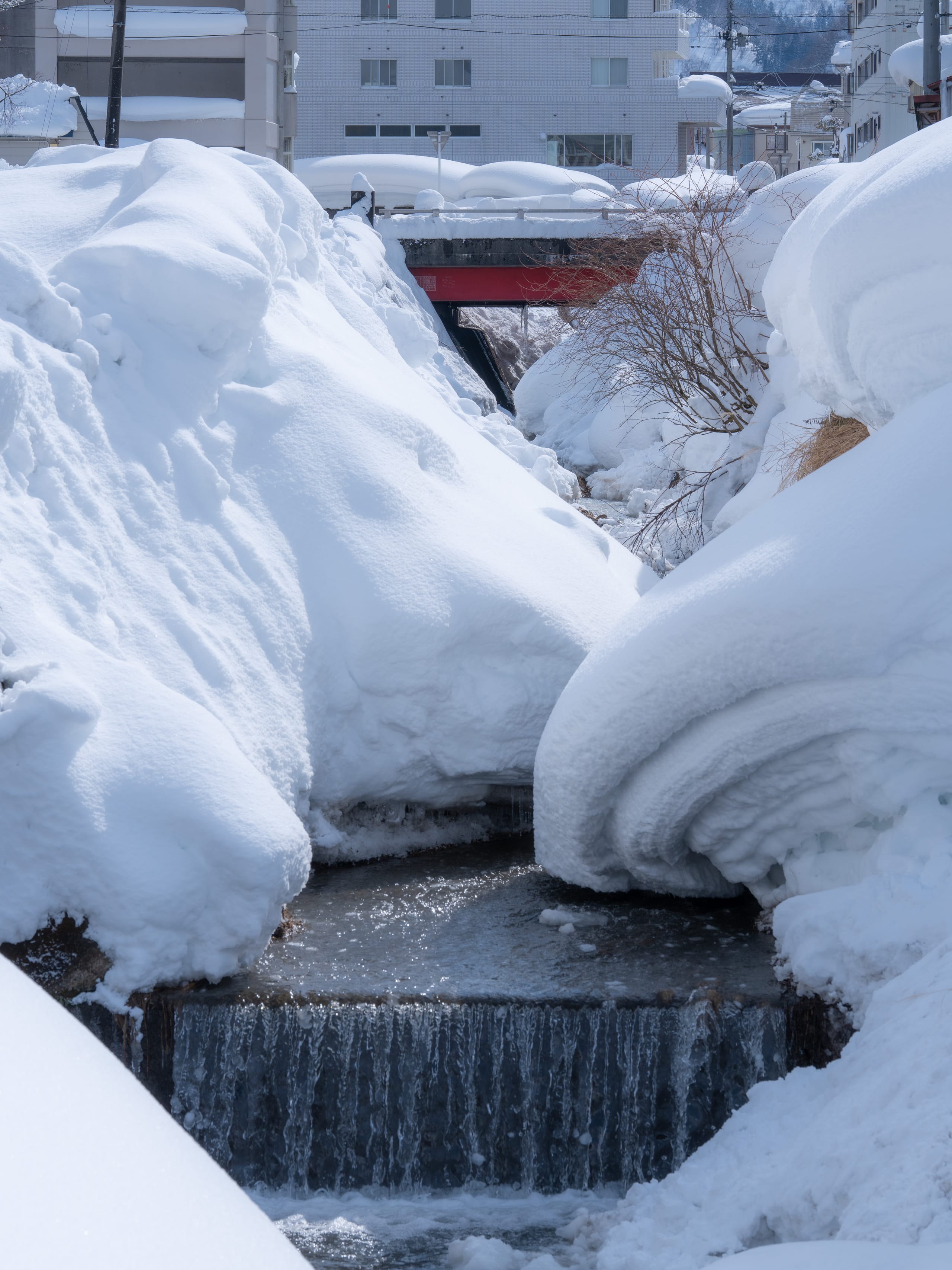 窄小溪流穿过两侧厚厚积雪和冰层。