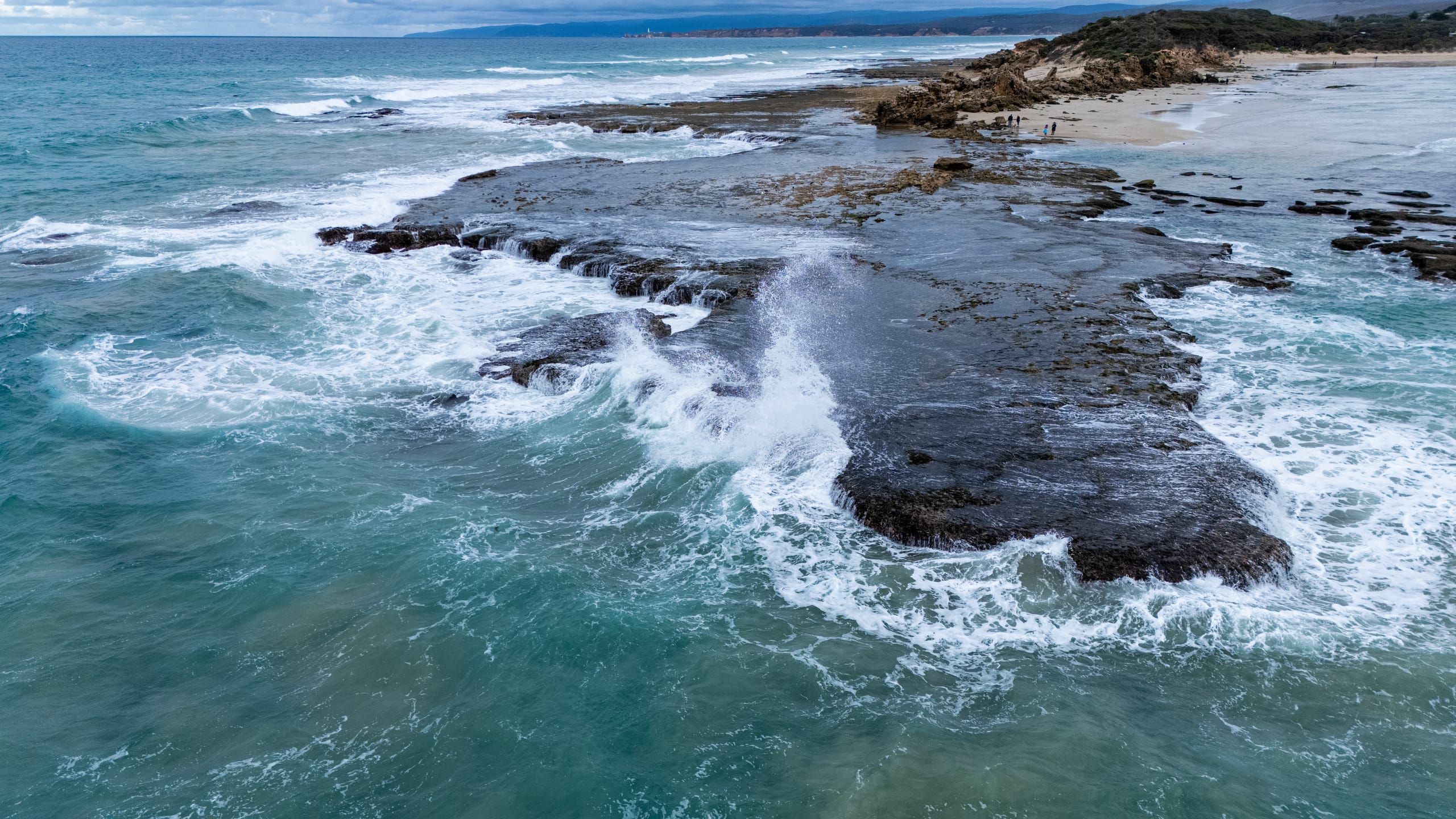 海浪越过深色岩石平台，白色泡沫铺满水面。