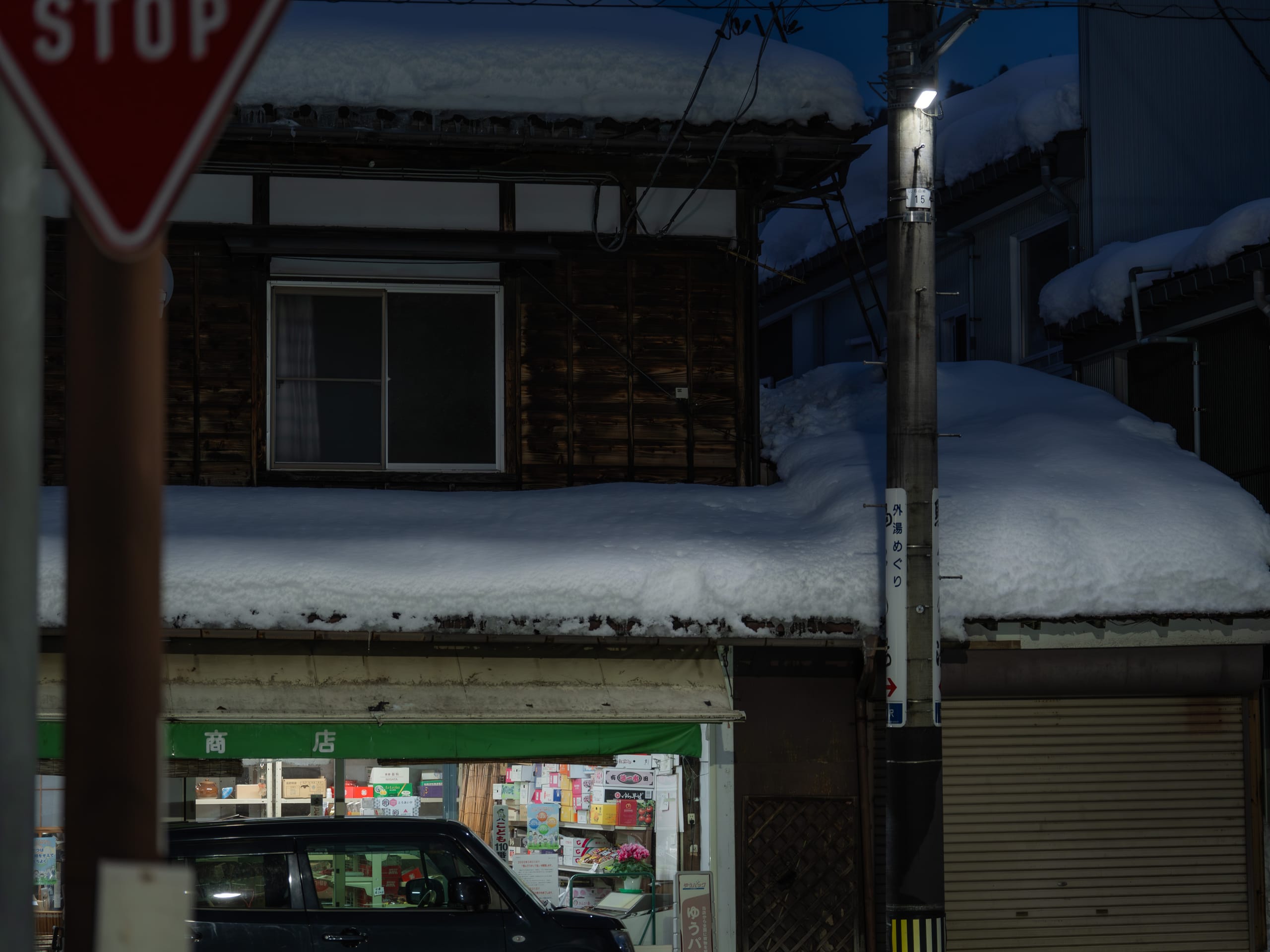 雪夜街角的小店亮着灯，屋顶和路边堆满积雪。