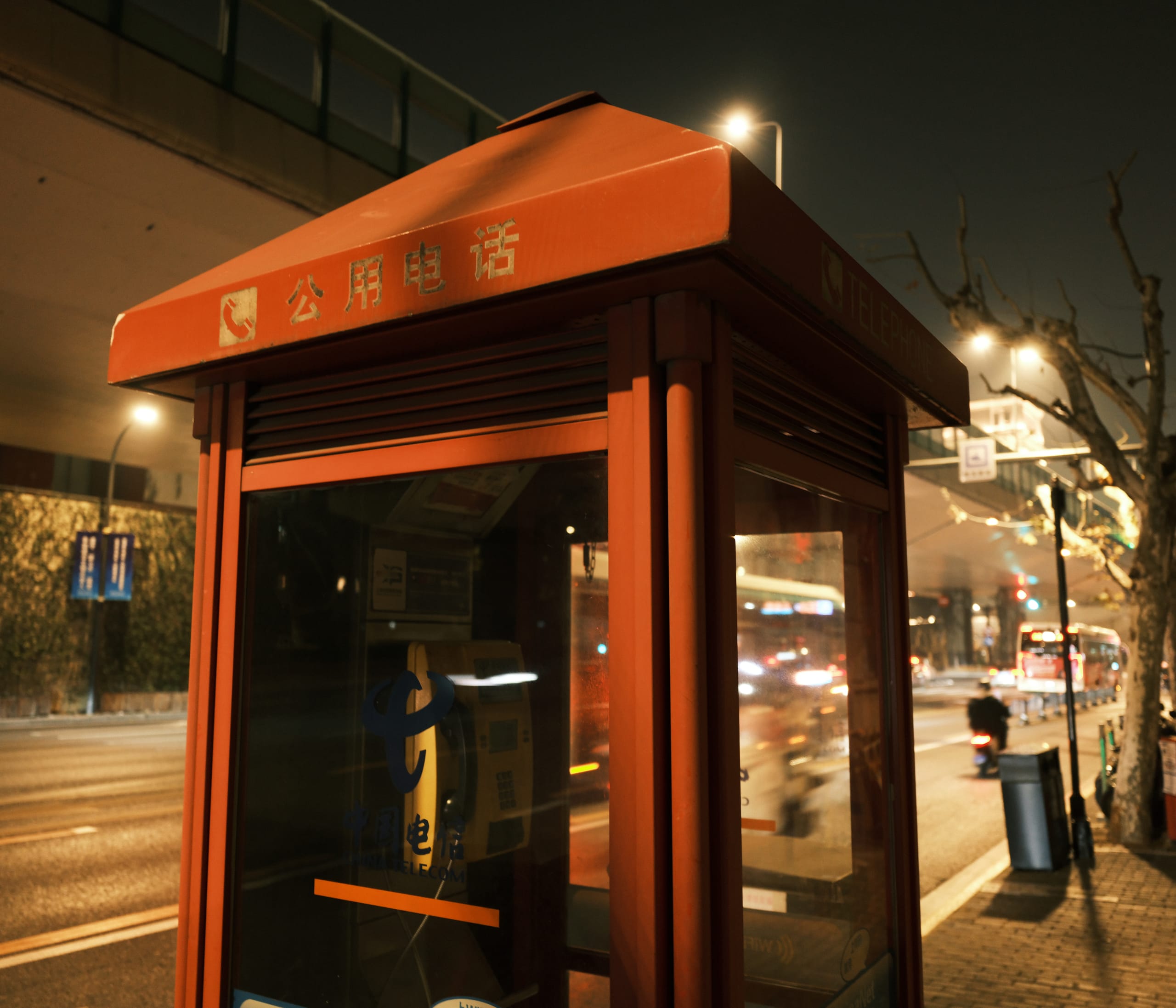 夜间街边一座红色站亭，周围路灯和店铺亮起。