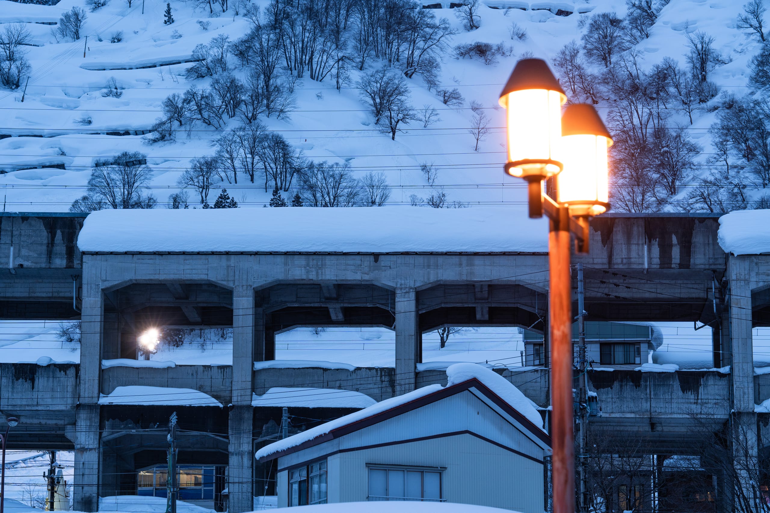 暖色街灯照亮雪夜小镇，远处山坡和楼房覆满白雪。