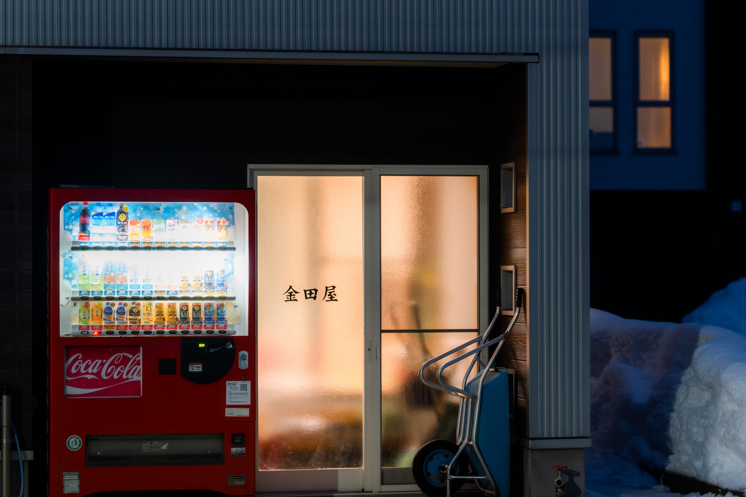 红色自动售货机与暖光门廊照亮深雪中的建筑入口。