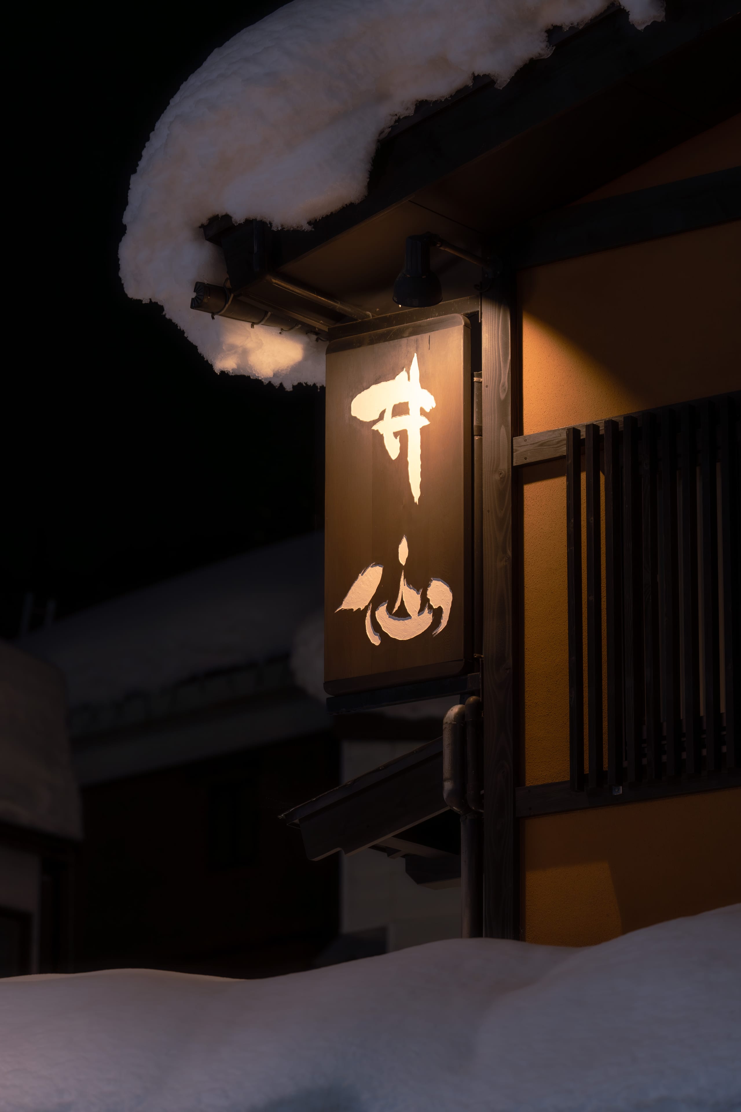夜色中一块暖光招牌悬在积雪覆盖的屋檐下。