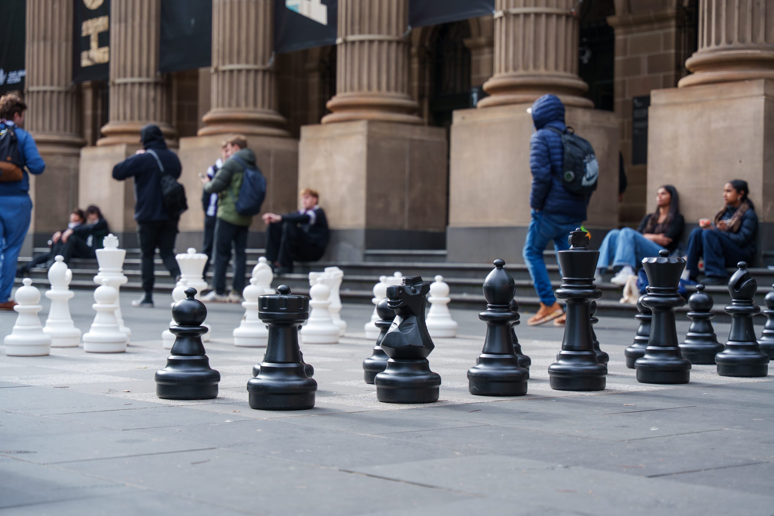 城市广场上的大型黑白棋子，行人在棋盘后方休息。