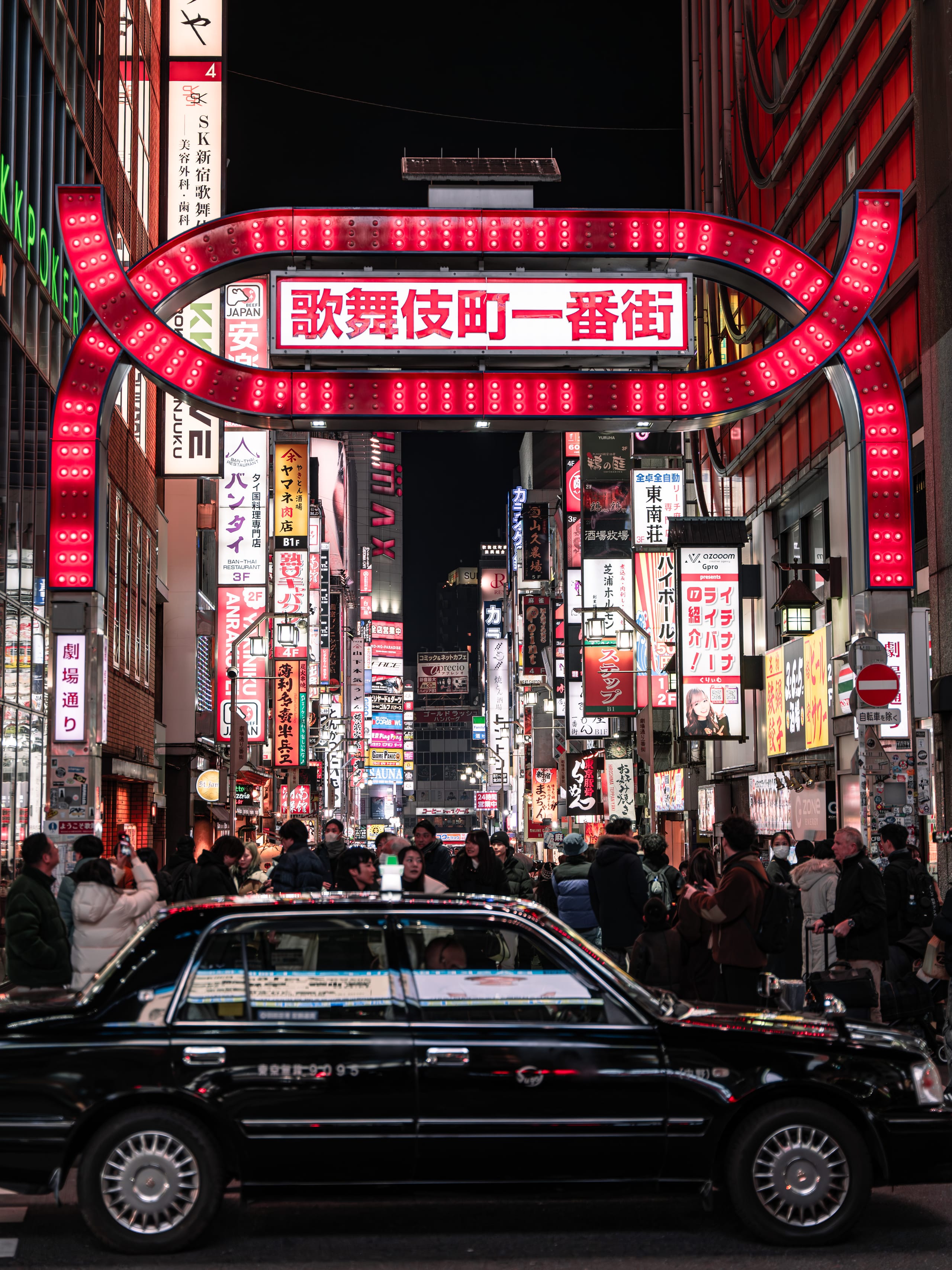 黑色出租车停在红色霓虹拱门下的夜间街道。