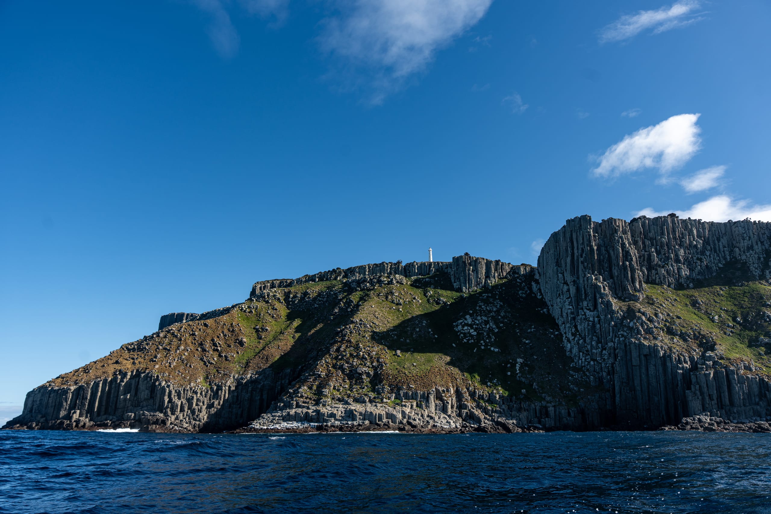 蓝天下一座陡峭岩岛从深色海面升起。
