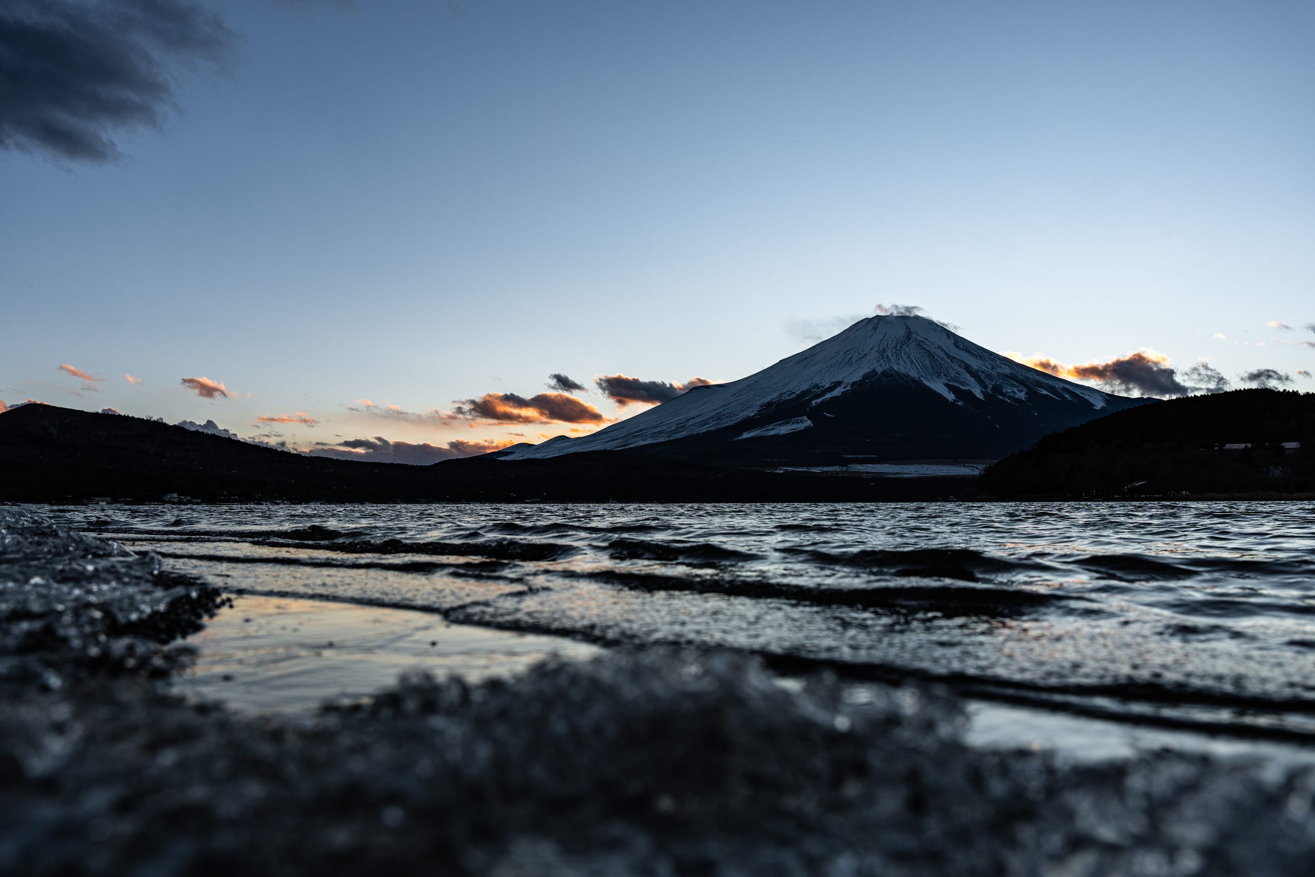 蓝灰湖水前方是覆雪山峰与低矮晚霞。