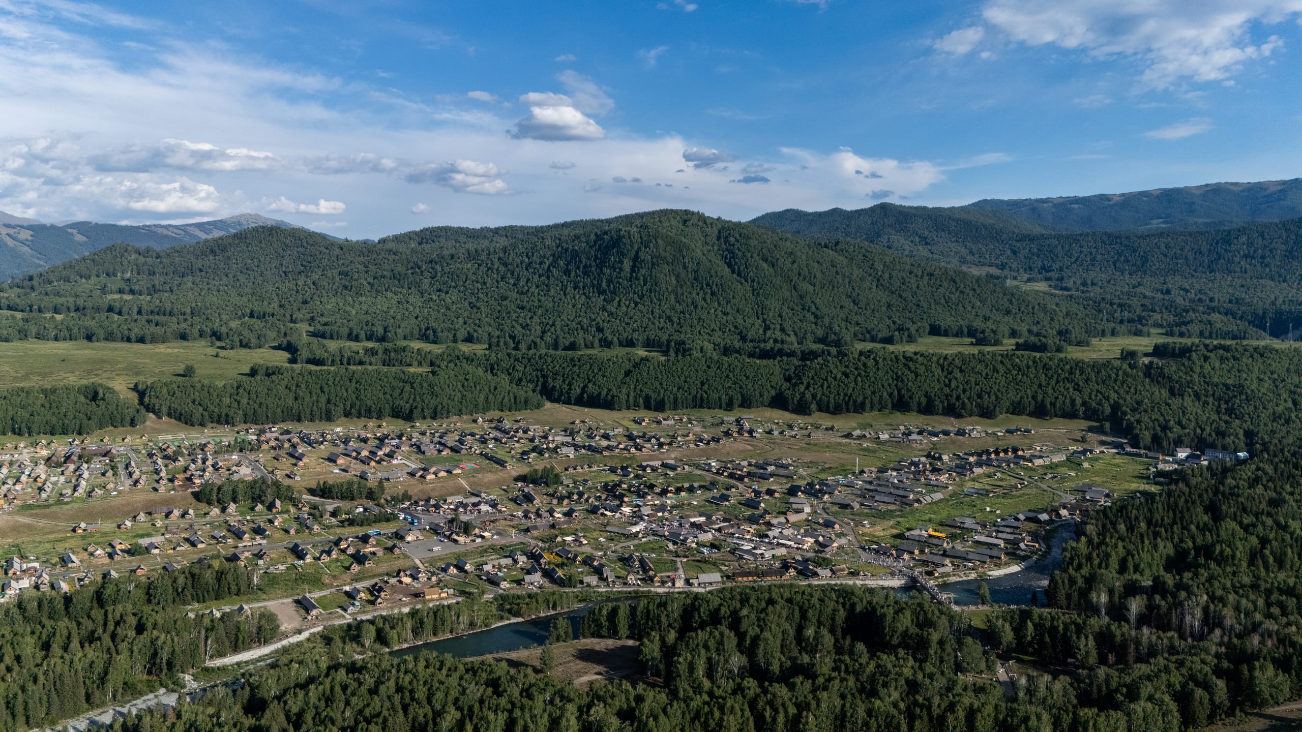 航拍禾木村，密集木屋沿道路排列在树林与山谷之间。