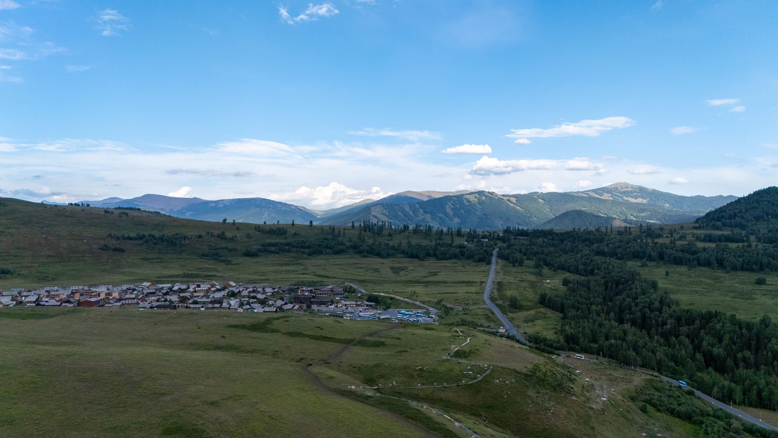 翻过禾木村后方山丘，开阔草地、道路与一片木屋聚落展现在群山前。