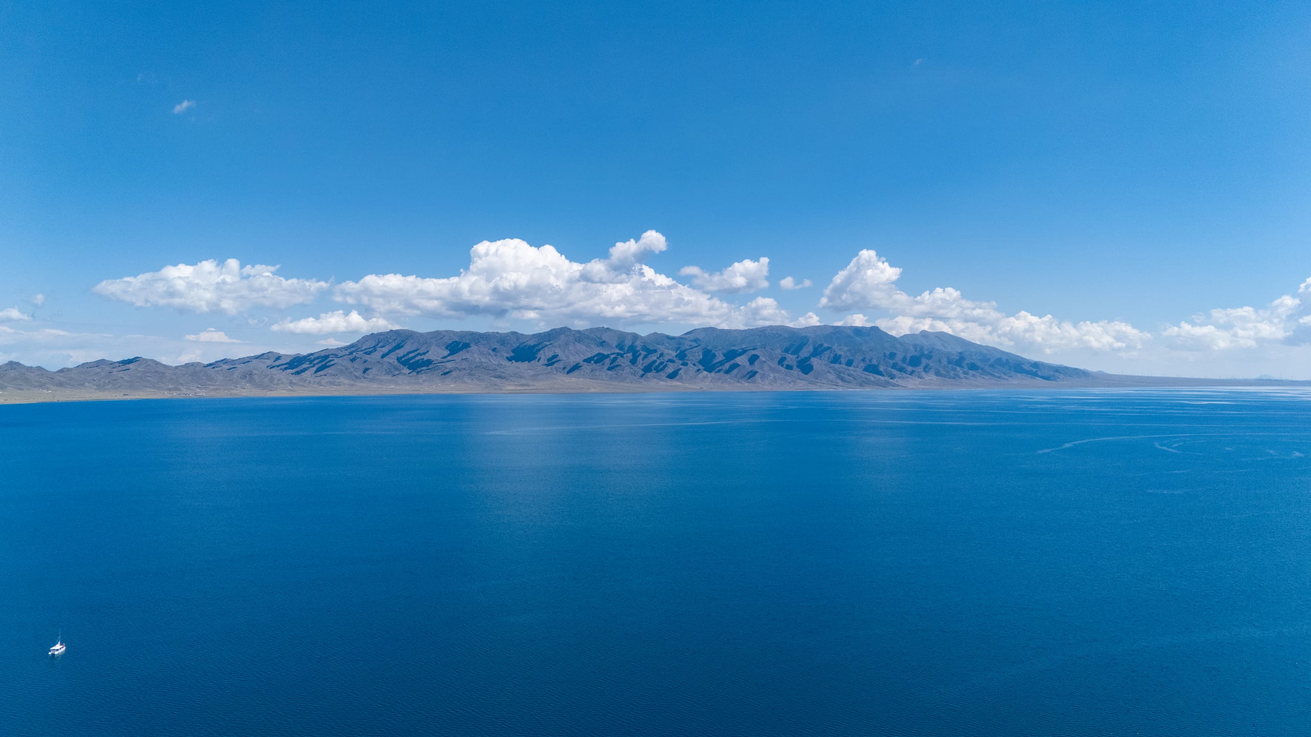 空中侧望赛里木湖，湖面由近处深蓝延伸到云下山脉。