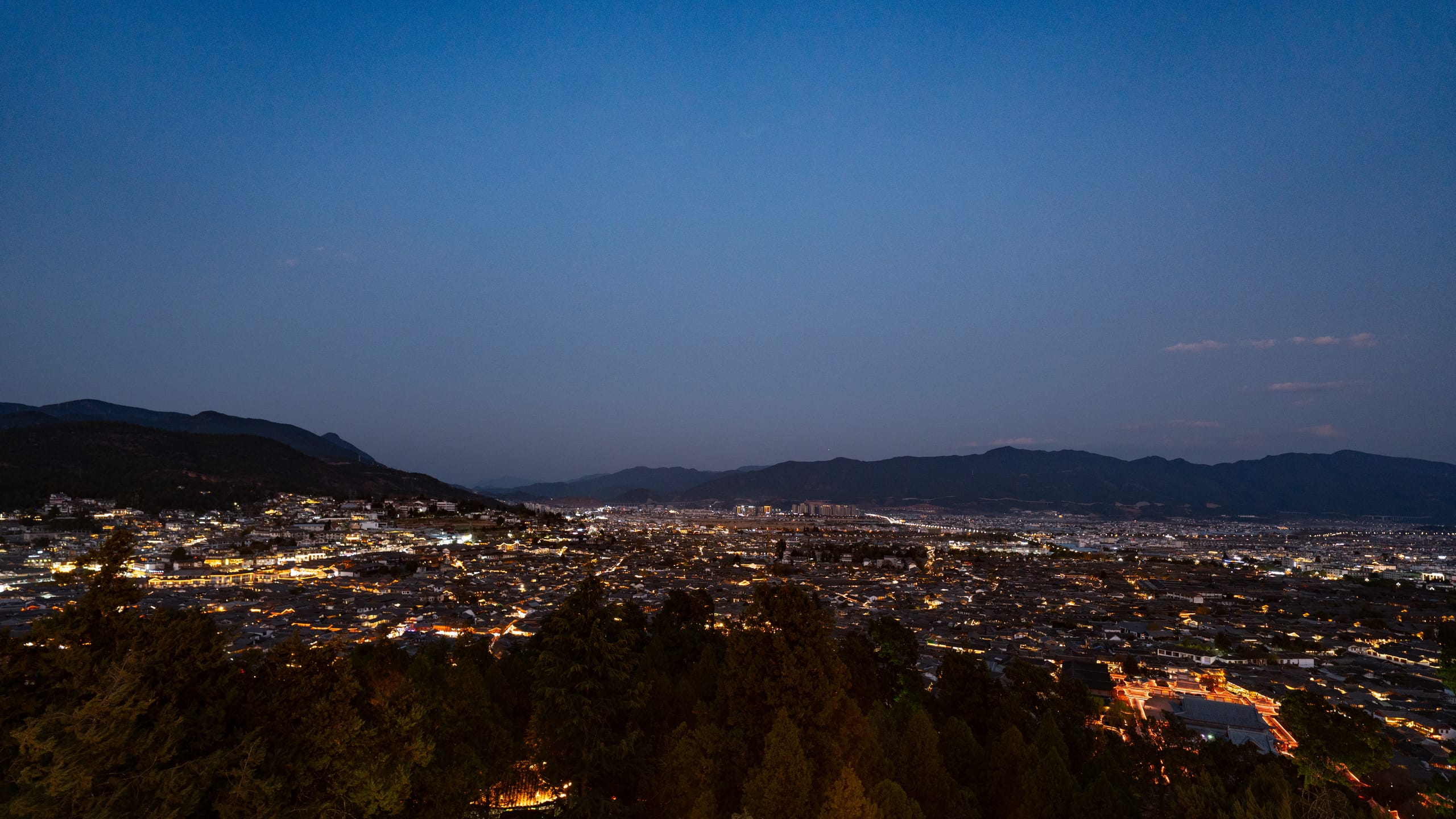 丽江古城夜景全景，密集灯火从山脚延伸至远处城区。