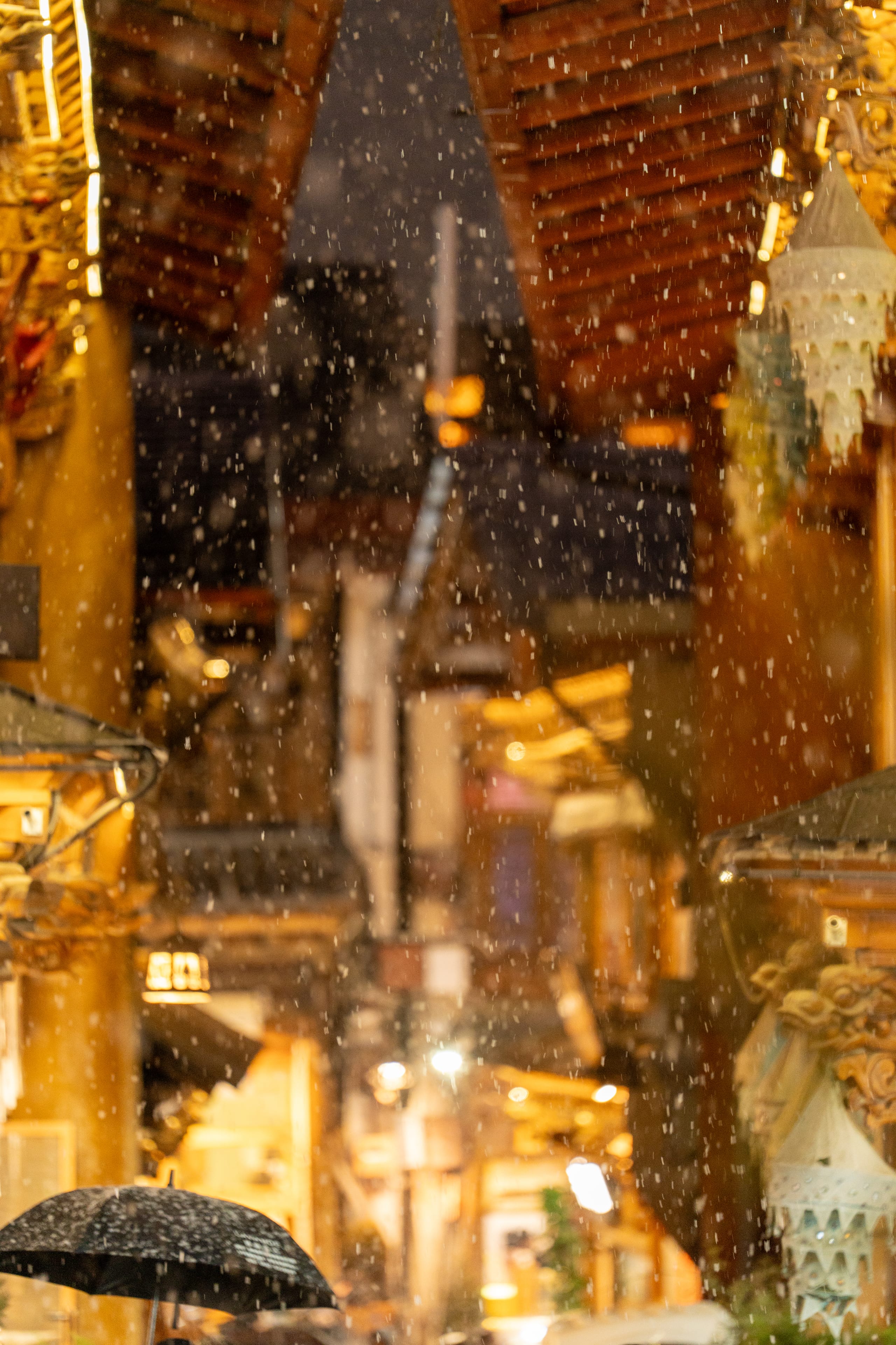 夜色中，雪花在独克宗古城暖黄灯光照亮的屋檐之间密集飘落。