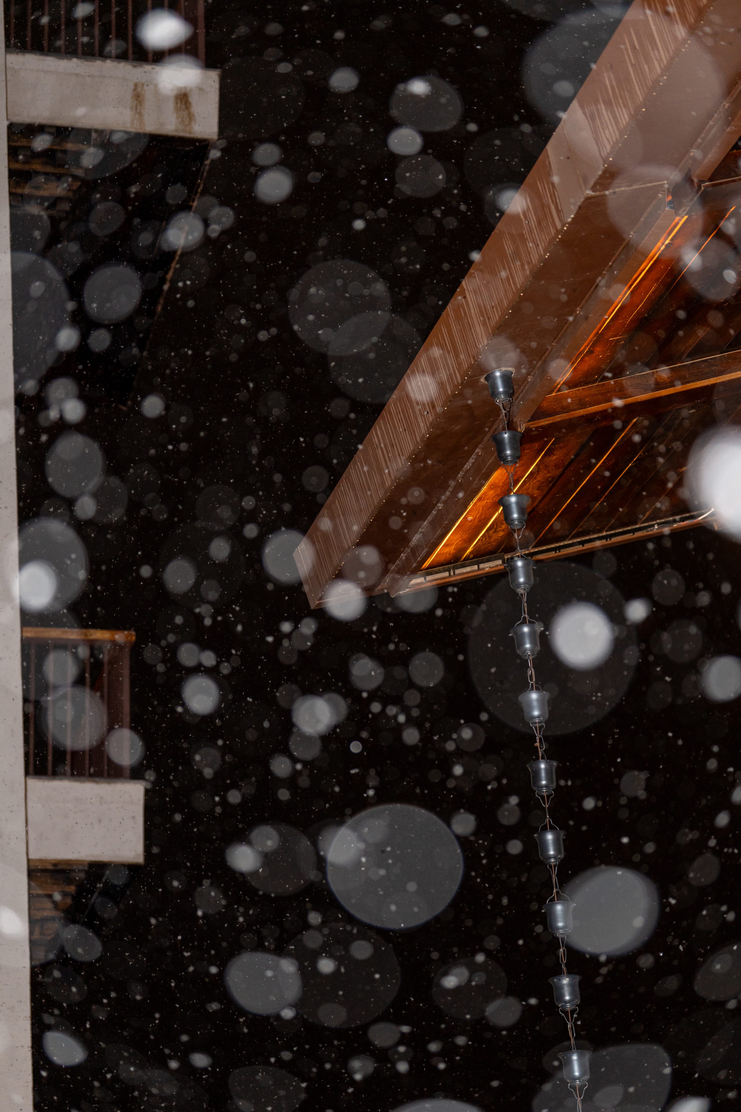 仰望木质屋檐，闪光灯照亮近处飞舞的雪花与屋角积雪。
