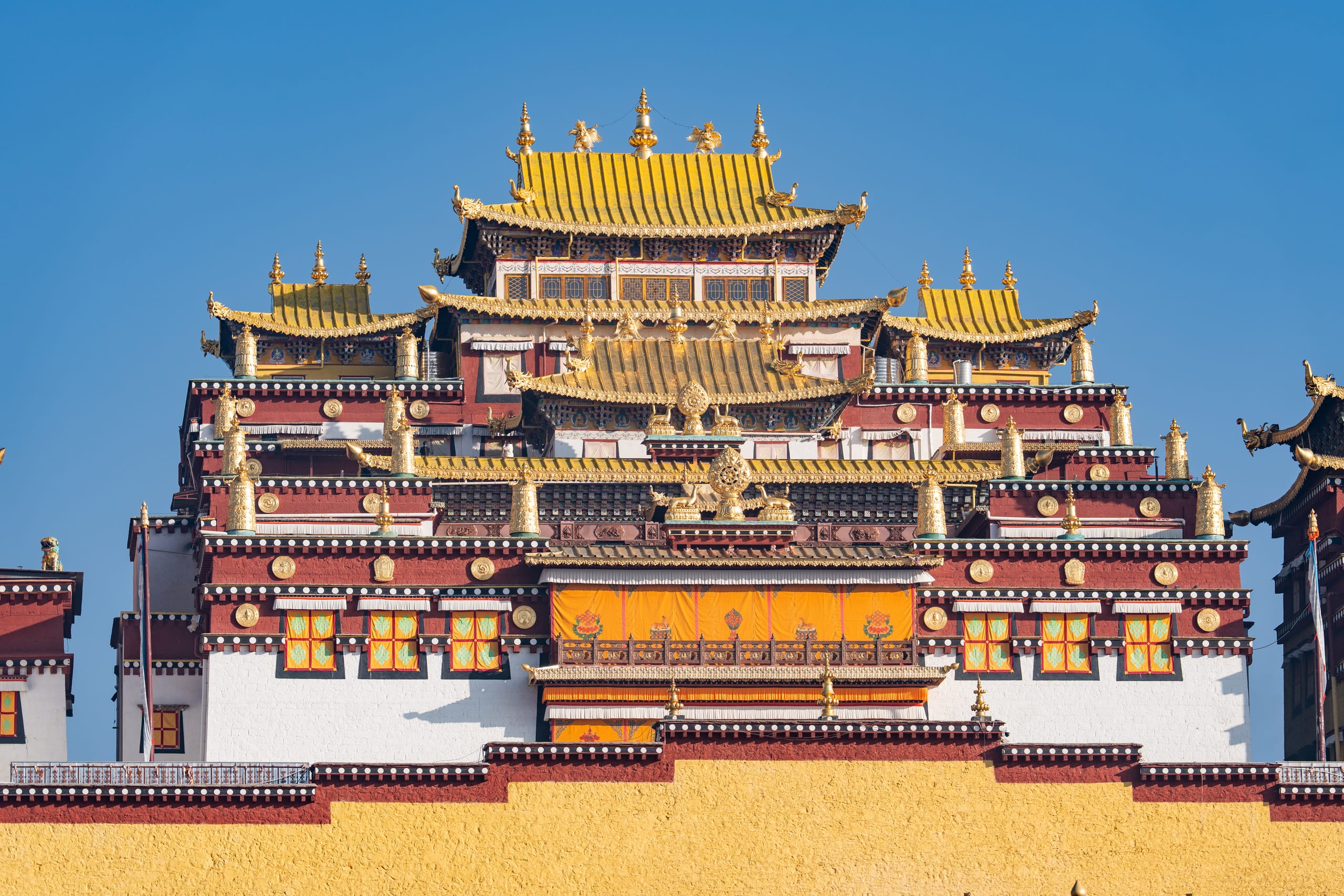 松赞林寺正面建筑在蓝天下展开，金色屋顶与彩色墙面层层向上。