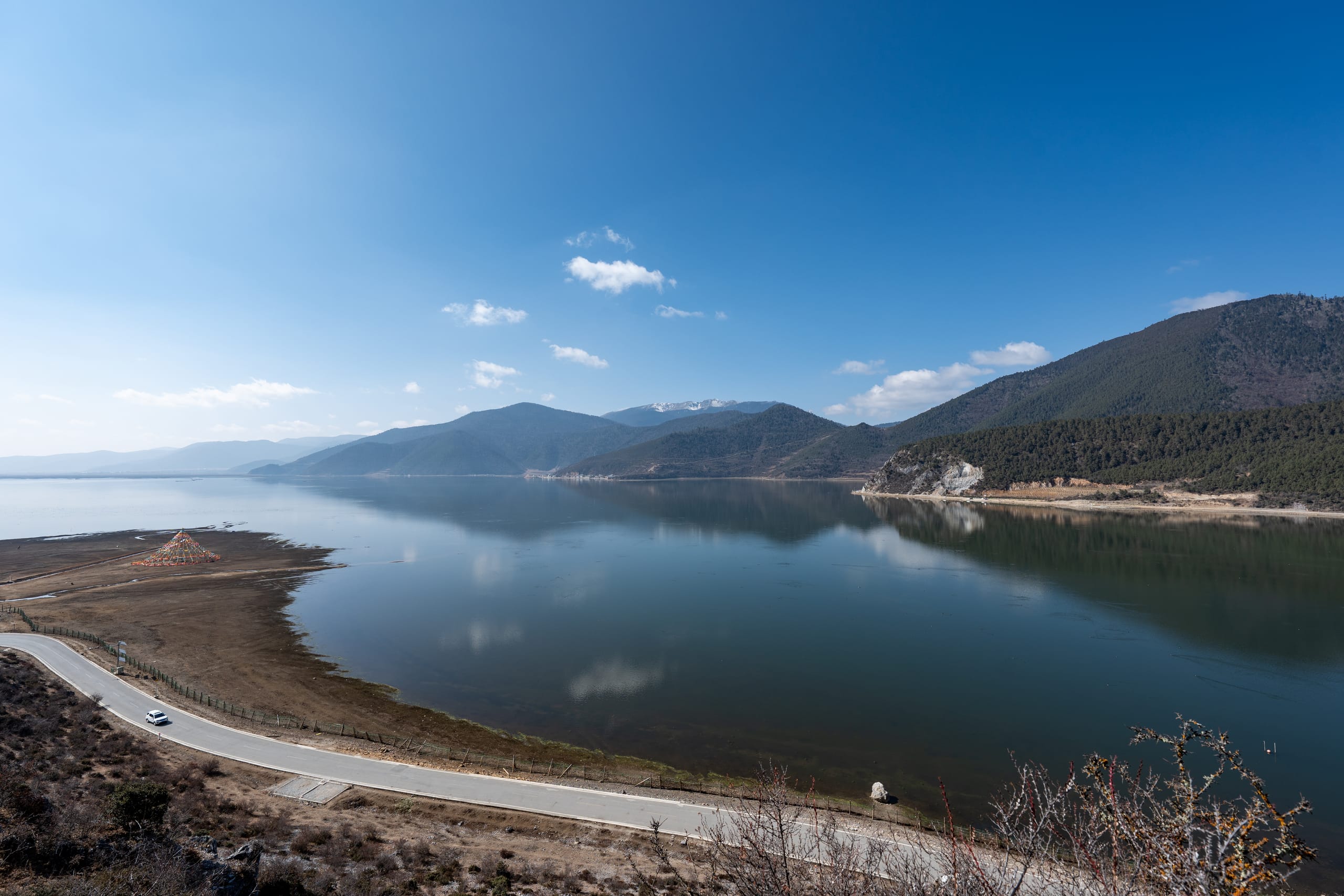 纳帕海弧形湖岸与山谷公路，平静水面映出蓝天和远山。