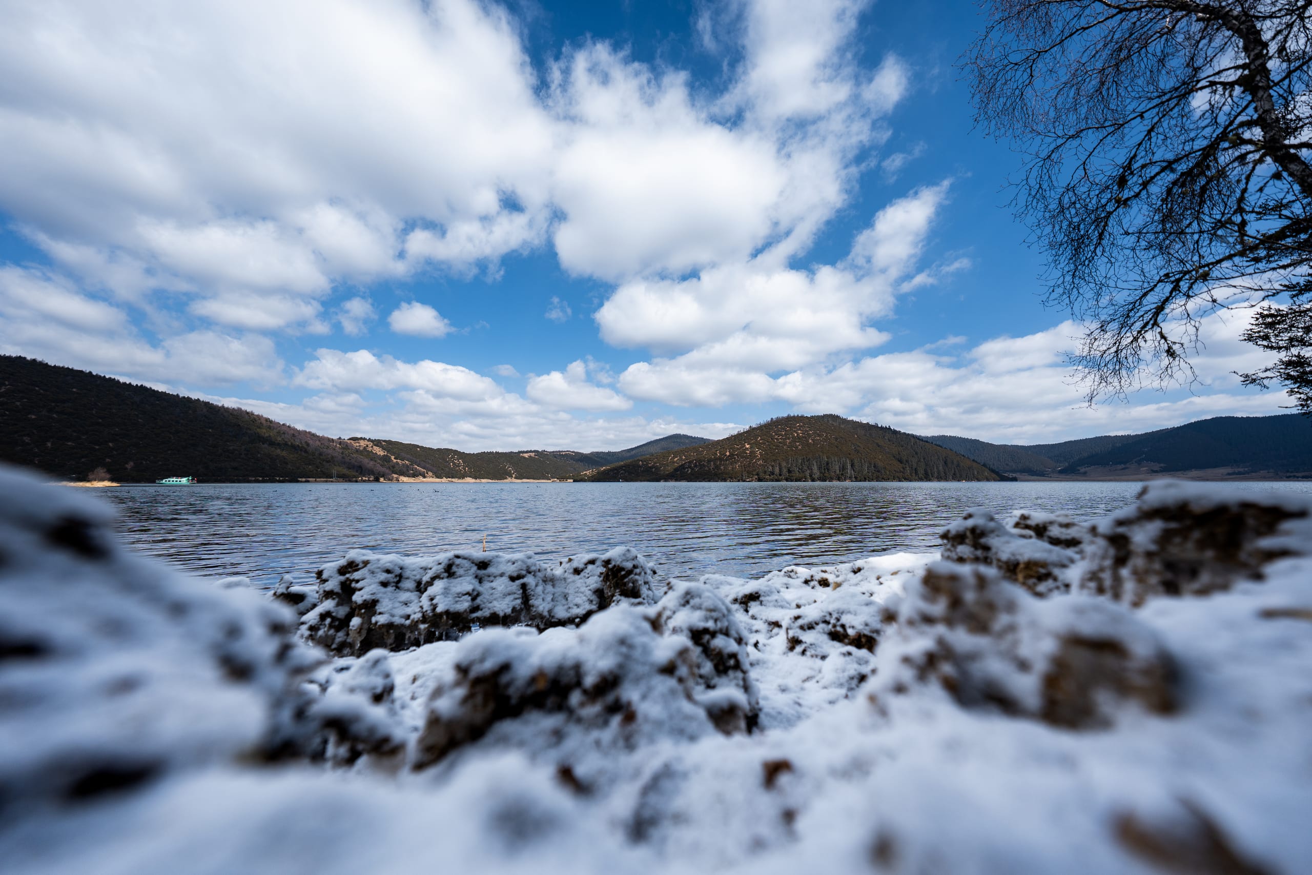 属都湖岸边覆着薄雪，水面与远山延伸在蓝天白云下。