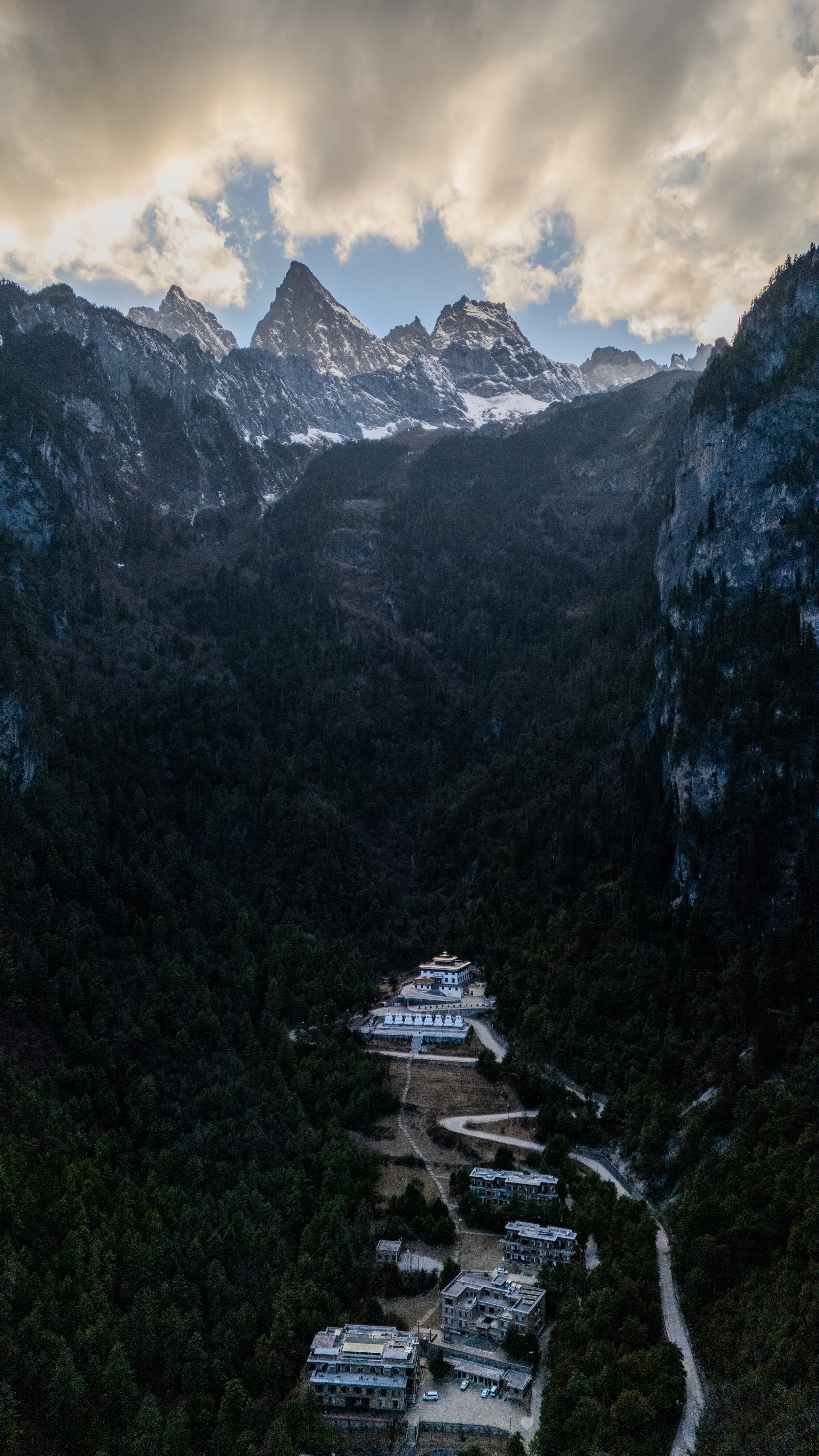 云雾笼罩格宗雪山尖峰，峡谷底部的白色建筑群显得微小。