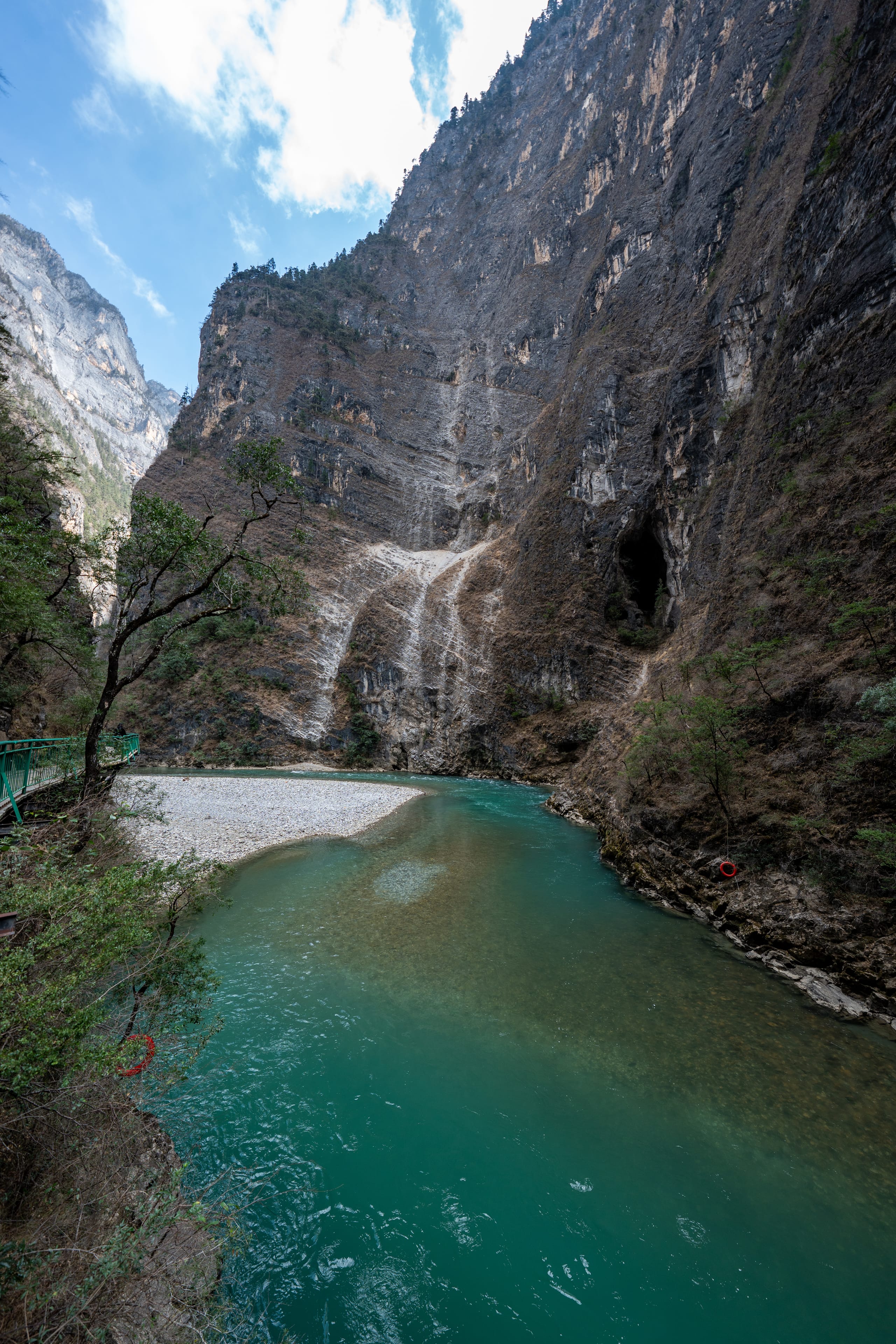 香格里拉大峡谷底部，碧绿色河流在高耸岩壁与小瀑布之间转弯。