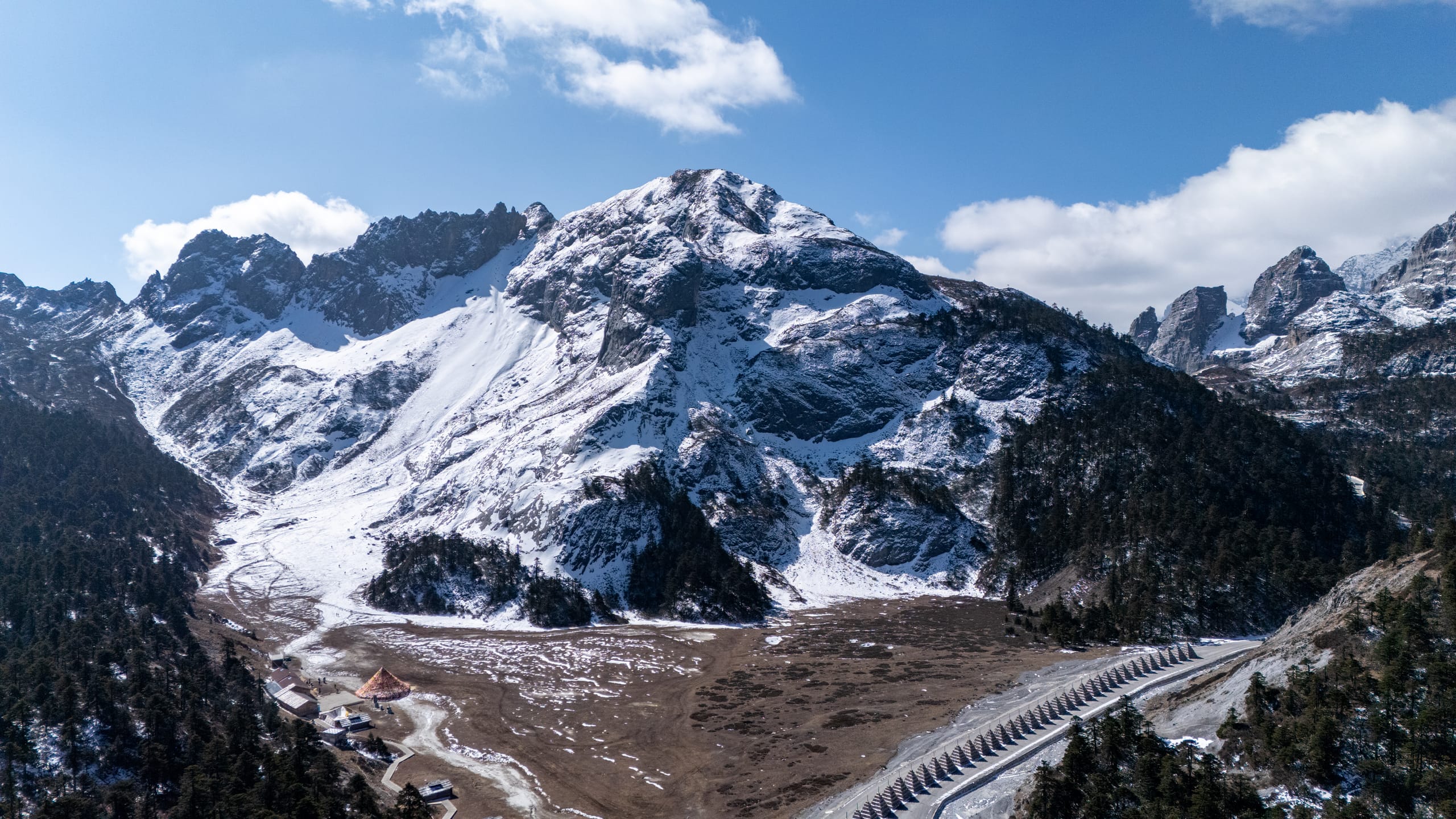 香巴拉佛塔前的连绵雪山横跨画面，山脚森林与道路形成弧线。