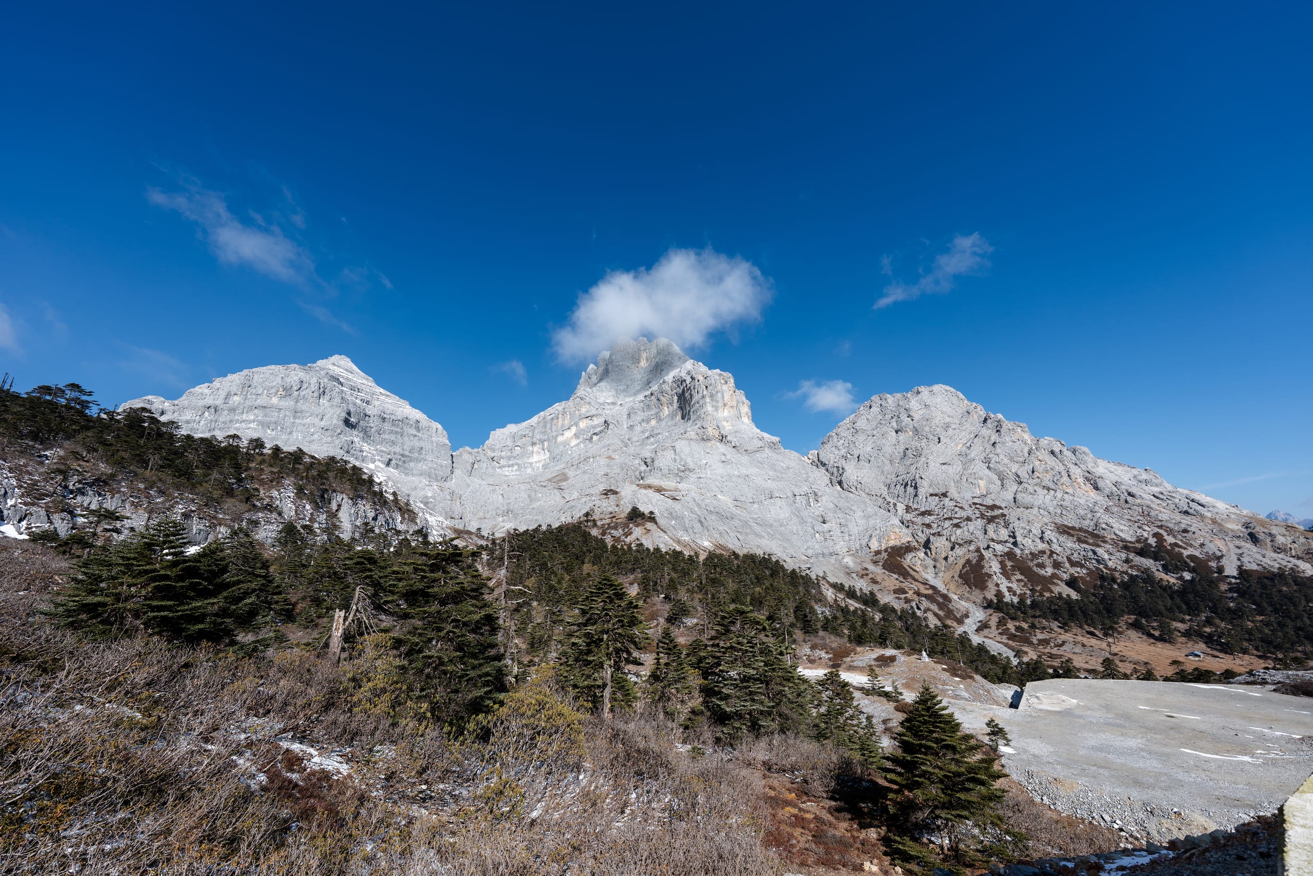 香巴拉佛塔白色峰群在蓝天下展开，坡脚稀疏树林与岩地相接。