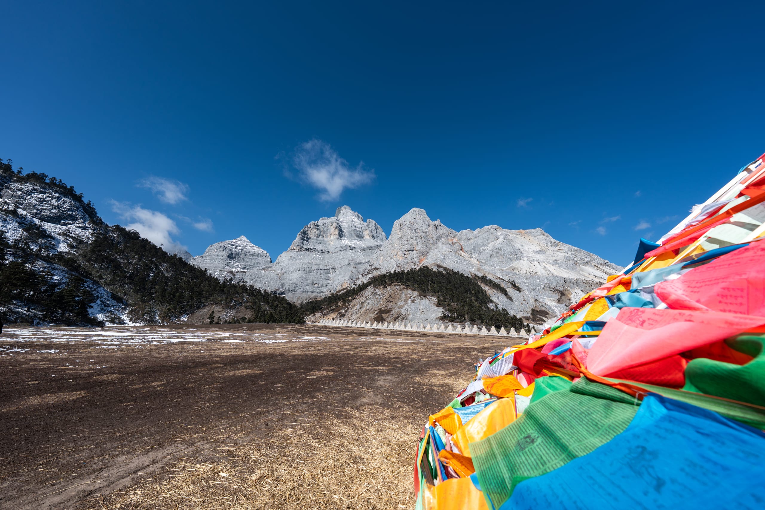 近处彩色经幡被风扬起，背后是香巴拉佛塔与覆雪群山。