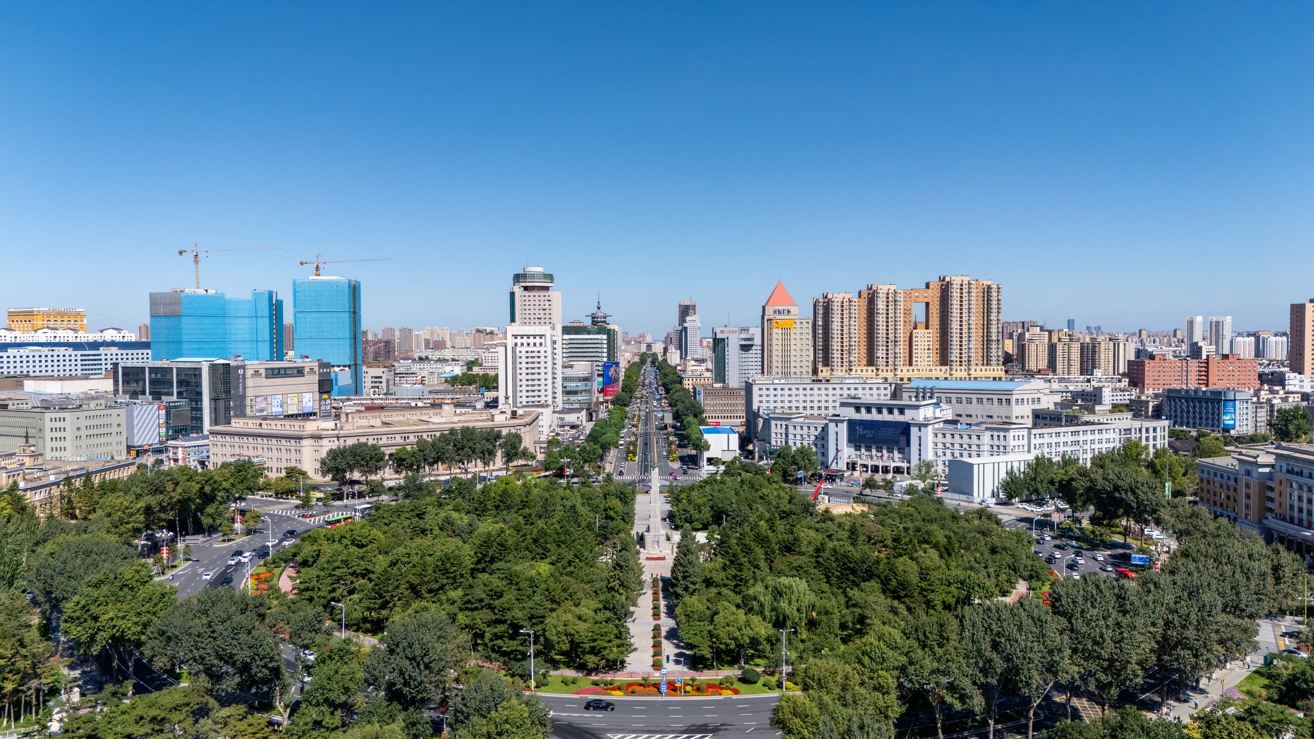 航拍人民广场，纪念碑、绿地和纵向道路位于城市建筑之间。