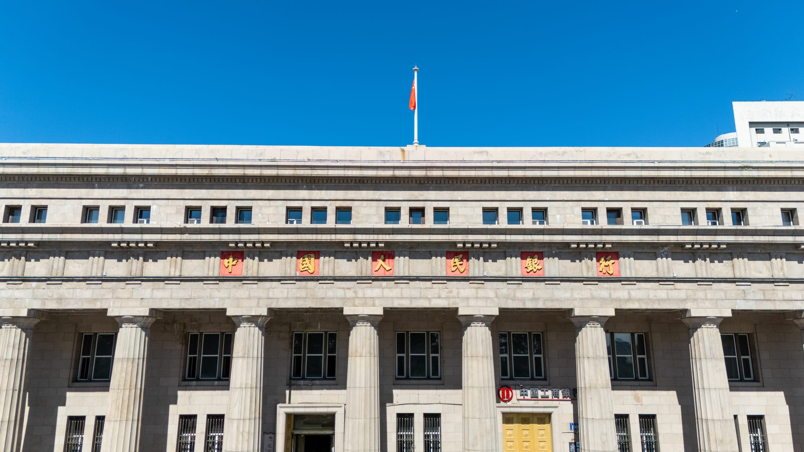 蓝天下的长春市人民政府建筑立面，屋顶升起一面红旗。