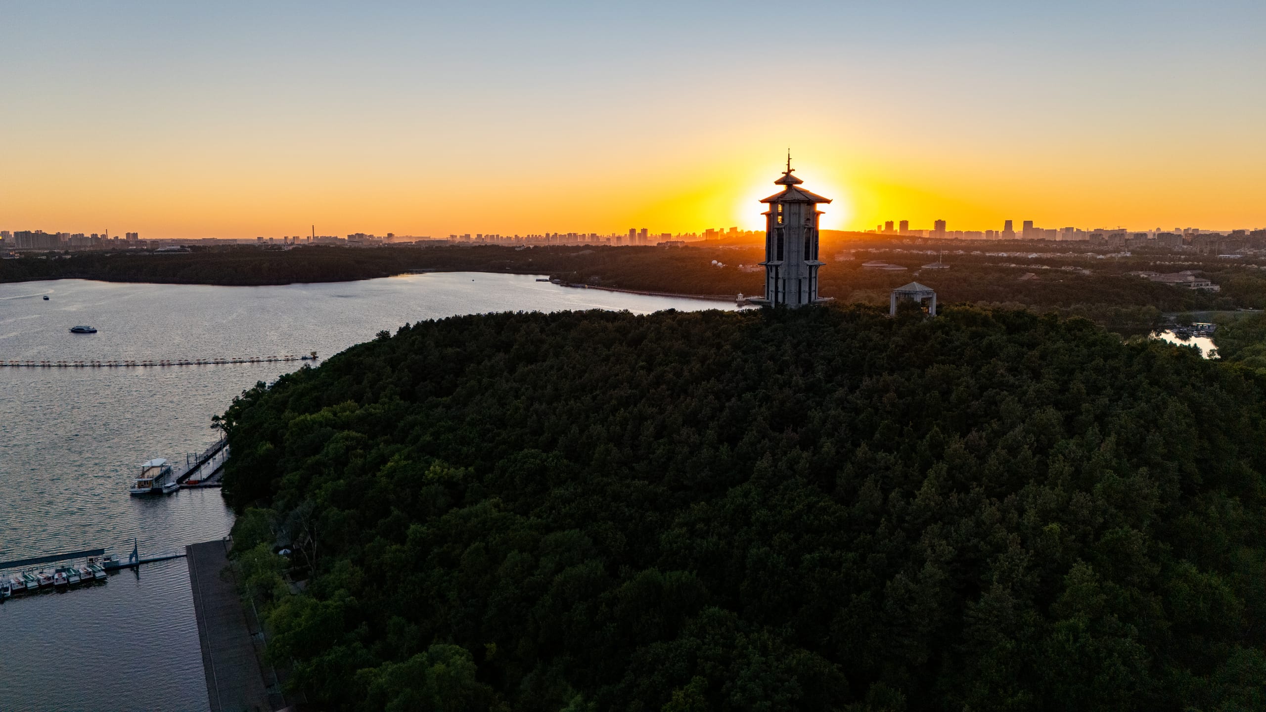 橙色夕阳落在净月潭远处天际，近岸亭楼成为剪影。